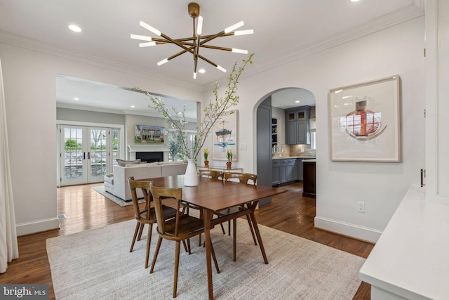 dining area featuring arched walkways, dark wood-type flooring, ornamental molding, recessed lighting, and baseboards