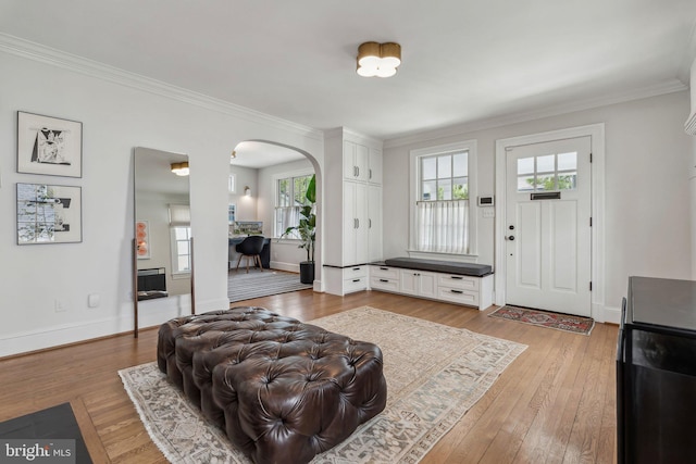 living area featuring arched walkways, plenty of natural light, crown molding, and wood-type flooring