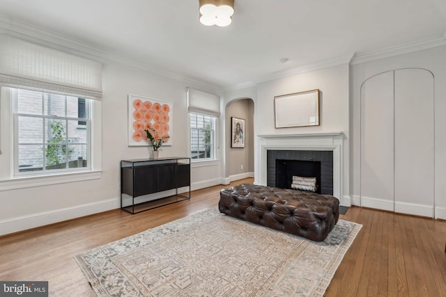living room with arched walkways, wood finished floors, crown molding, a fireplace, and baseboards