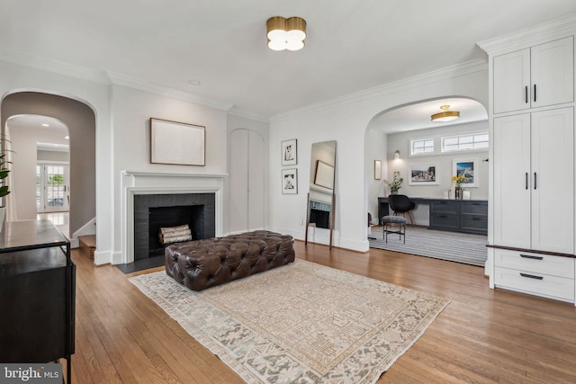 living area with a fireplace, arched walkways, wood finished floors, and ornamental molding