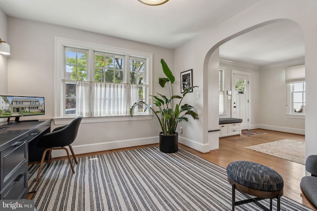 home office featuring arched walkways, baseboards, and wood finished floors