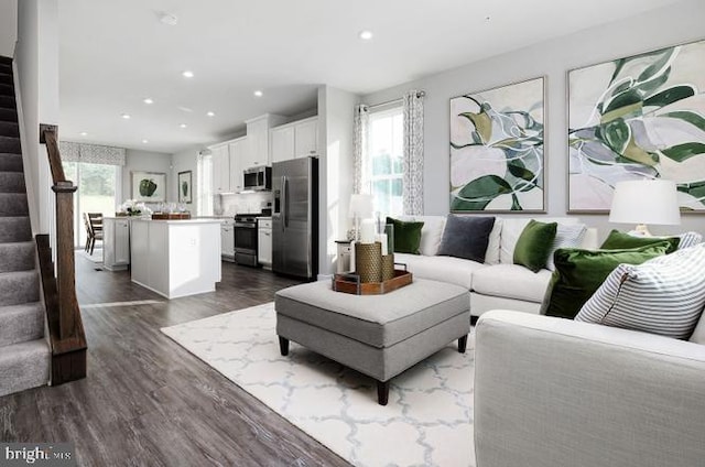 living room with a wealth of natural light, stairway, recessed lighting, and dark wood-style flooring