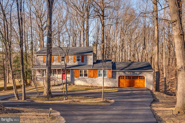 view of front of house with an attached garage, a chimney, and driveway