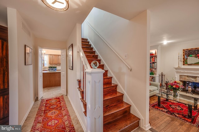 staircase with wood finished floors, a fireplace, visible vents, and baseboards