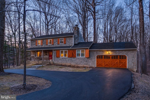 view of front of home with aphalt driveway, an attached garage, a chimney, and a porch