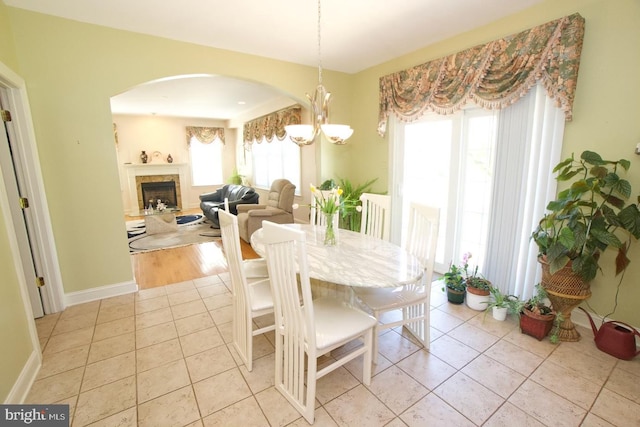 dining area with light tile patterned floors, baseboards, a fireplace, arched walkways, and a notable chandelier