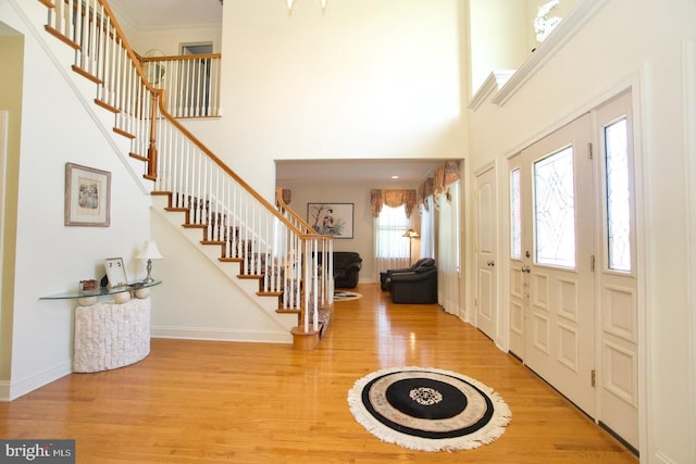 entrance foyer featuring baseboards, a high ceiling, stairs, light wood-style floors, and crown molding