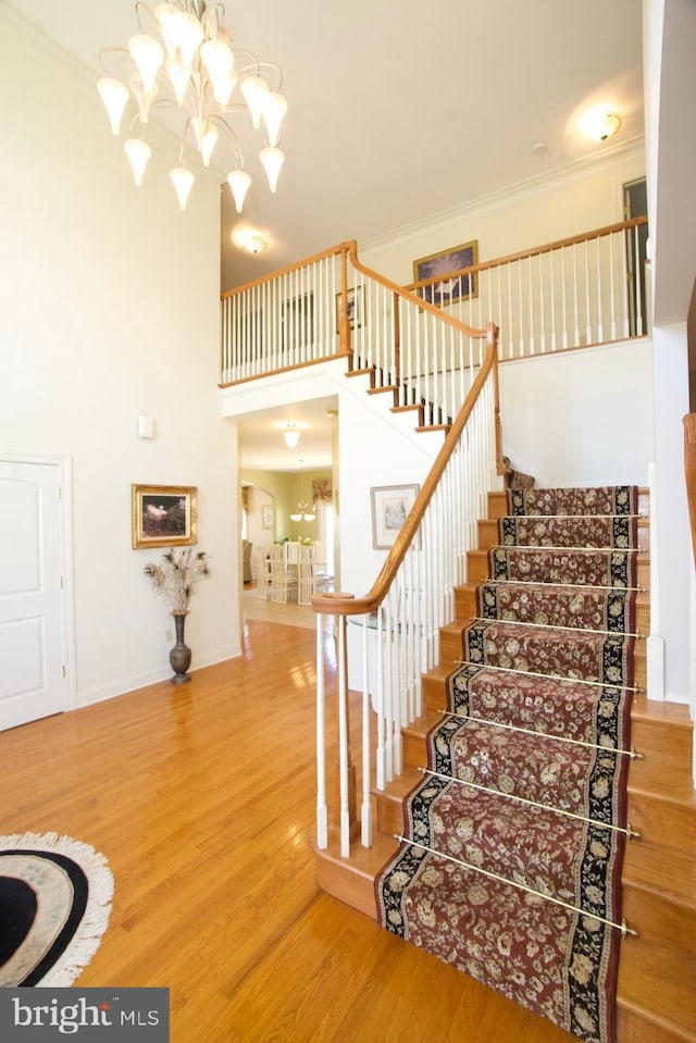 staircase with baseboards, wood finished floors, ornamental molding, a towering ceiling, and an inviting chandelier