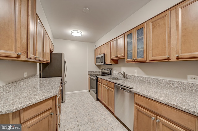 kitchen featuring a sink, light stone counters, appliances with stainless steel finishes, light tile patterned flooring, and glass insert cabinets