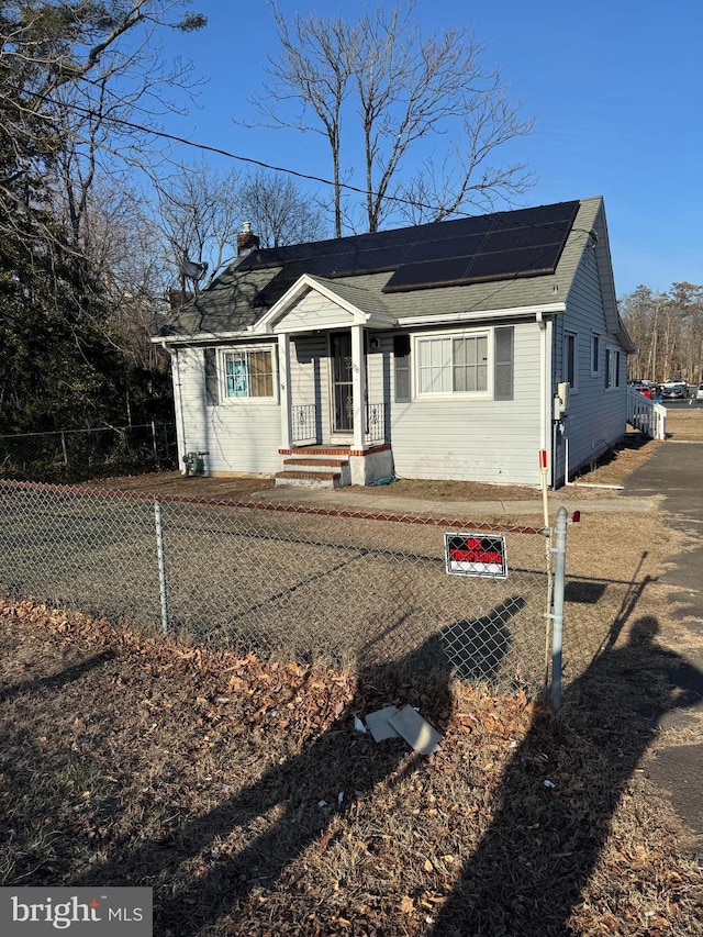 bungalow-style house with a fenced front yard, roof mounted solar panels, and a chimney