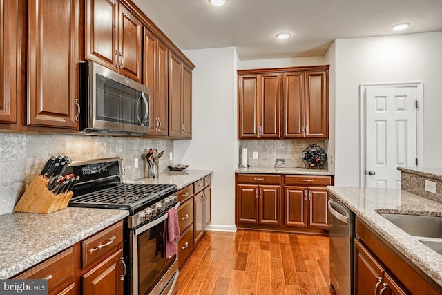 kitchen featuring backsplash, light stone counters, brown cabinets, appliances with stainless steel finishes, and light wood-style floors