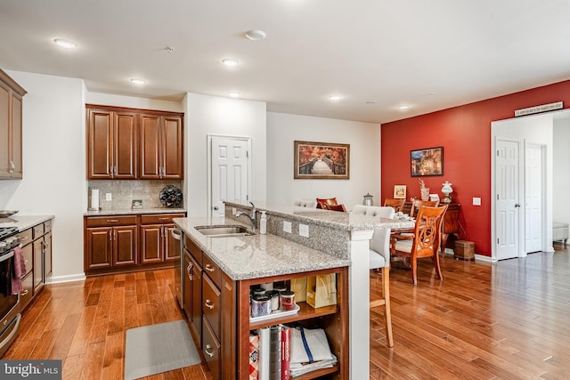 kitchen featuring light stone countertops, light wood-type flooring, a kitchen bar, stainless steel appliances, and a sink