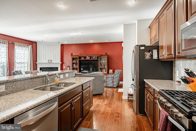 kitchen with a sink, wood finished floors, a large fireplace, appliances with stainless steel finishes, and decorative backsplash