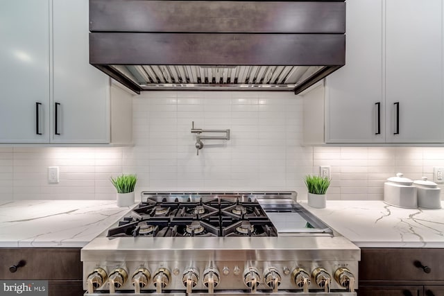 kitchen with wall chimney range hood, light stone counters, stainless steel range with gas stovetop, and backsplash