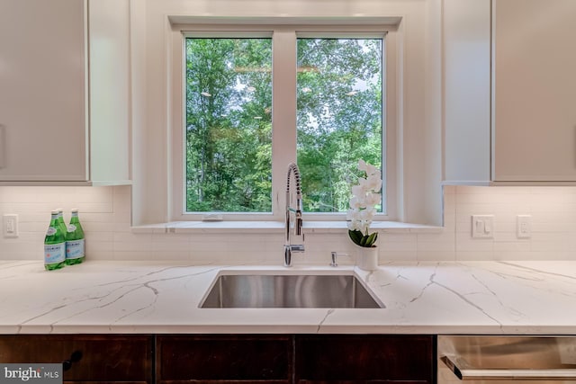 kitchen featuring a sink, dishwashing machine, light stone countertops, and backsplash