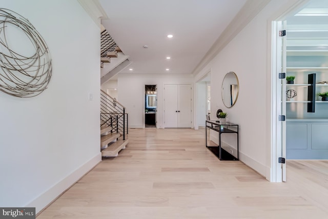 corridor featuring light wood-type flooring, ornamental molding, recessed lighting, baseboards, and stairs