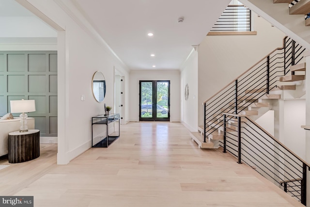 foyer featuring a decorative wall, french doors, stairs, and ornamental molding