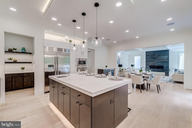 kitchen with an island with sink, recessed lighting, a sink, built in appliances, and light wood-type flooring