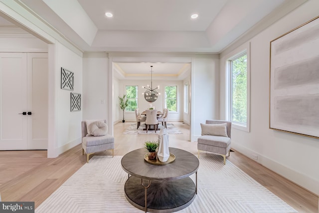 living area with baseboards, an inviting chandelier, a tray ceiling, ornamental molding, and light wood-type flooring