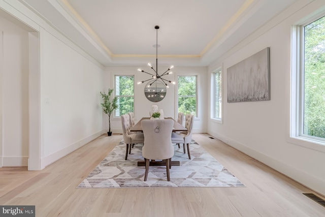 dining space with a tray ceiling, light wood-style flooring, plenty of natural light, and visible vents