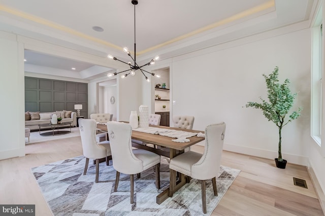 dining space featuring visible vents, a raised ceiling, an inviting chandelier, and light wood finished floors