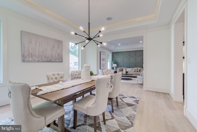 dining area featuring a notable chandelier, baseboards, light wood-type flooring, and a tray ceiling