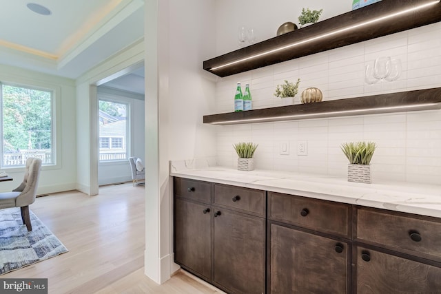 bar with tasteful backsplash, light wood finished floors, crown molding, and baseboards