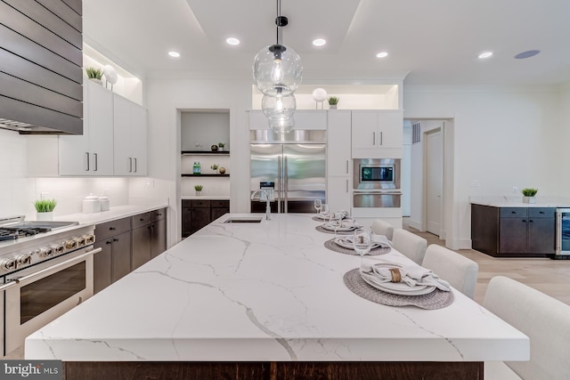 kitchen with a center island with sink, a sink, extractor fan, built in appliances, and crown molding