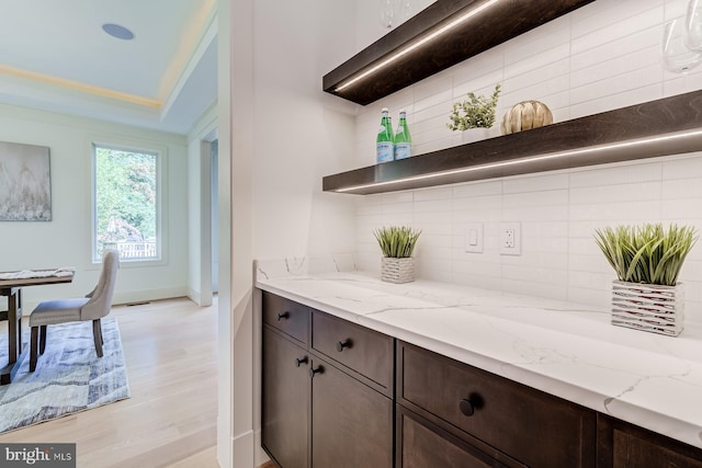 kitchen with open shelves, decorative backsplash, light stone countertops, and dark brown cabinetry