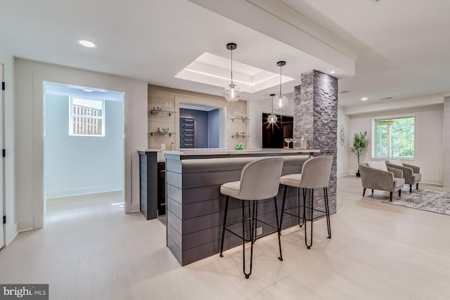 bar with bar area, baseboards, pendant lighting, light wood-type flooring, and a raised ceiling