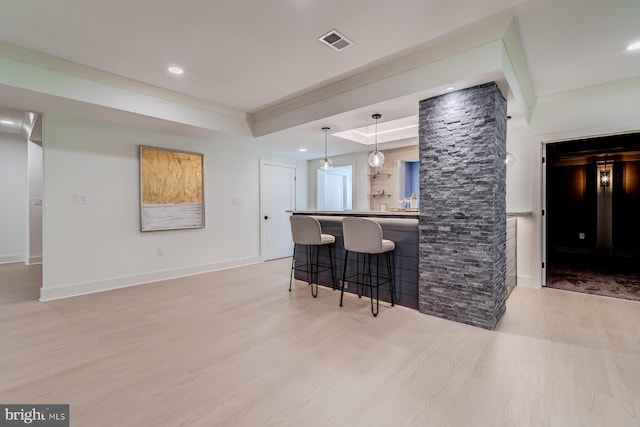 kitchen featuring a kitchen bar, visible vents, light wood-style floors, a peninsula, and baseboards