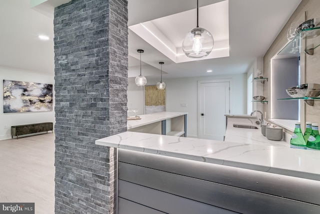 kitchen featuring decorative light fixtures, light stone counters, wood finished floors, a raised ceiling, and a sink