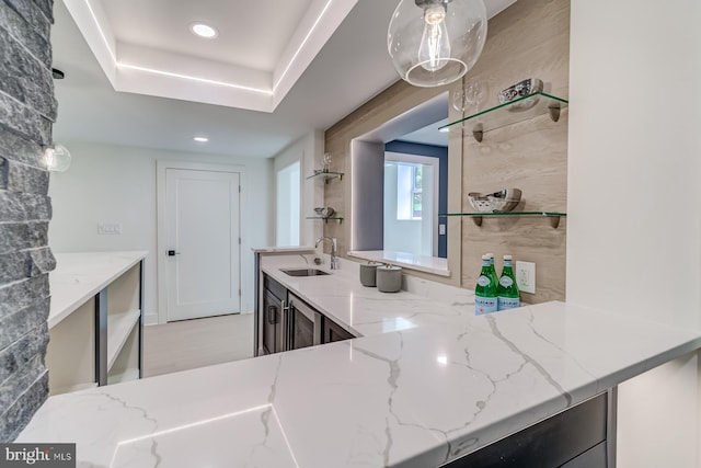 kitchen with a sink, light stone countertops, a raised ceiling, and recessed lighting