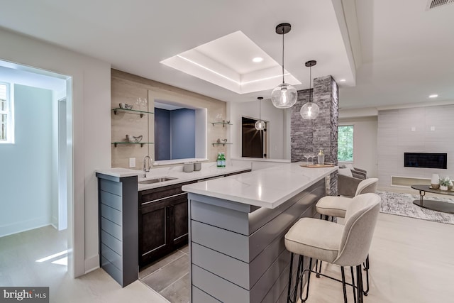 kitchen featuring light stone countertops, a premium fireplace, a sink, pendant lighting, and a kitchen bar