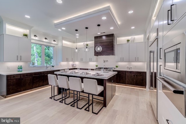 kitchen with oven, a breakfast bar, a center island with sink, wall chimney range hood, and dark brown cabinets