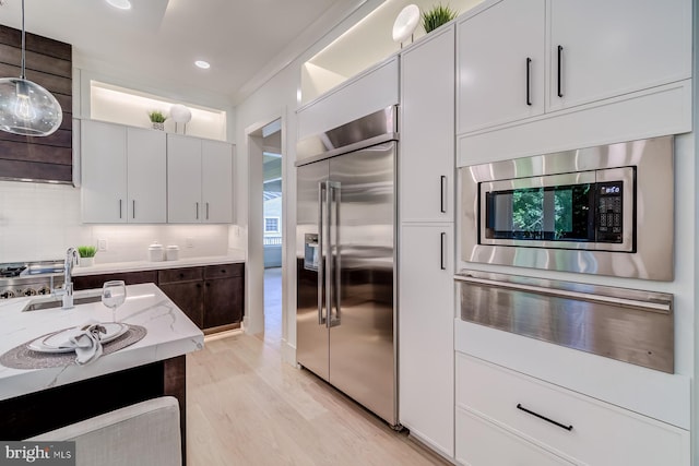 kitchen with a warming drawer, light stone counters, light wood-style floors, decorative backsplash, and built in appliances