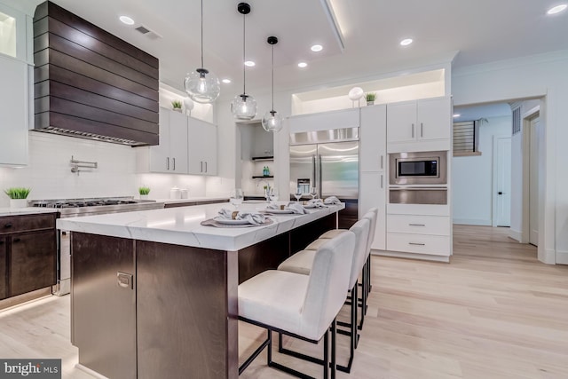 kitchen featuring visible vents, custom range hood, tasteful backsplash, a center island, and built in appliances