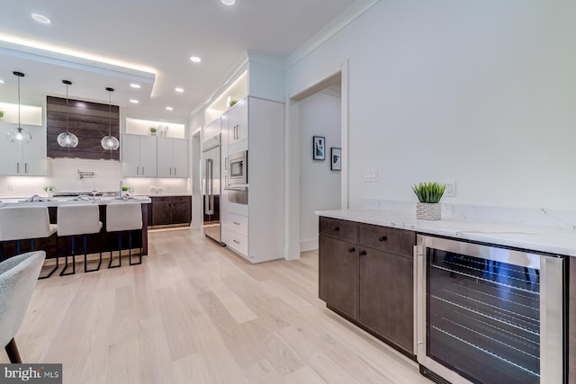 kitchen featuring tasteful backsplash, beverage cooler, built in appliances, dark brown cabinetry, and light wood-style floors