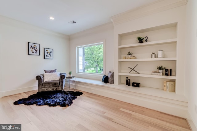 sitting room with built in features, wood finished floors, baseboards, visible vents, and ornamental molding