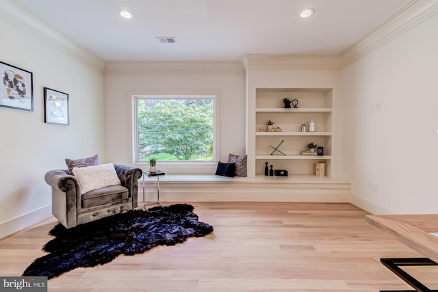 living area with visible vents, built in shelves, crown molding, and wood finished floors