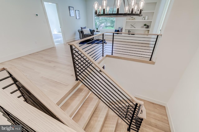 stairs featuring baseboards, an inviting chandelier, and wood finished floors