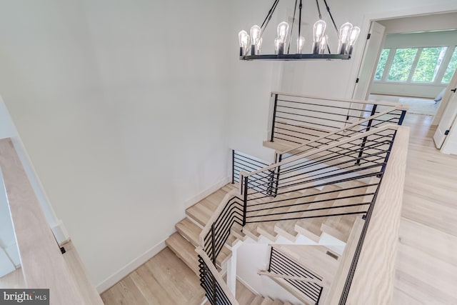 stairs with a notable chandelier, wood finished floors, and baseboards