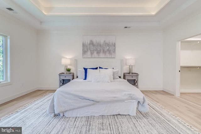 bedroom with a tray ceiling, baseboards, visible vents, and wood finished floors