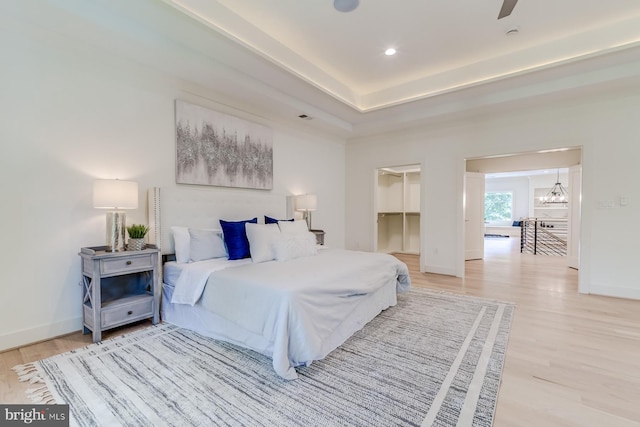 bedroom featuring recessed lighting, a tray ceiling, baseboards, and light wood-style floors