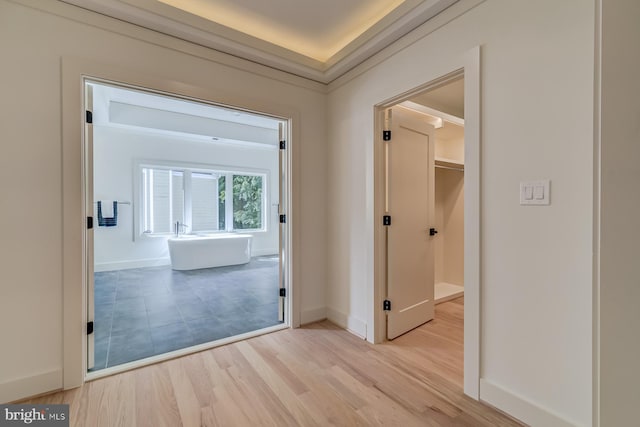 hallway featuring crown molding, light wood-type flooring, and baseboards