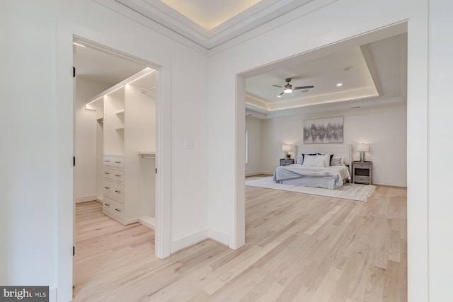 bedroom with a tray ceiling, crown molding, light wood finished floors, baseboards, and a spacious closet