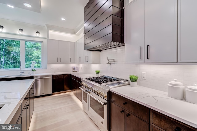 kitchen with dark brown cabinets, backsplash, light stone counters, appliances with stainless steel finishes, and custom exhaust hood