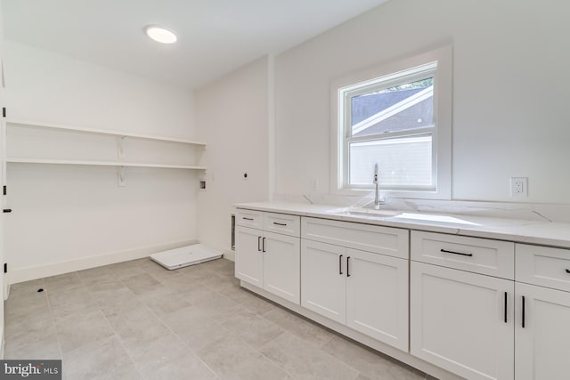 interior space featuring light stone countertops, white cabinetry, baseboards, and a sink