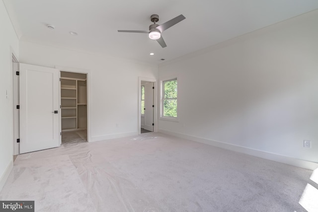 unfurnished bedroom featuring a spacious closet, crown molding, ceiling fan, baseboards, and carpet floors