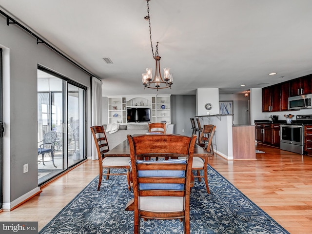 dining space featuring light wood-style flooring, a notable chandelier, visible vents, and baseboards